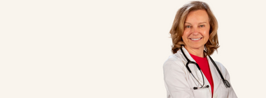Smiling female doctor (Dr. Elizabeth Klodas) with shoulder-length blonde hair wearing a white lab coat and red top, with a stethoscope around her neck, standing against a light background.