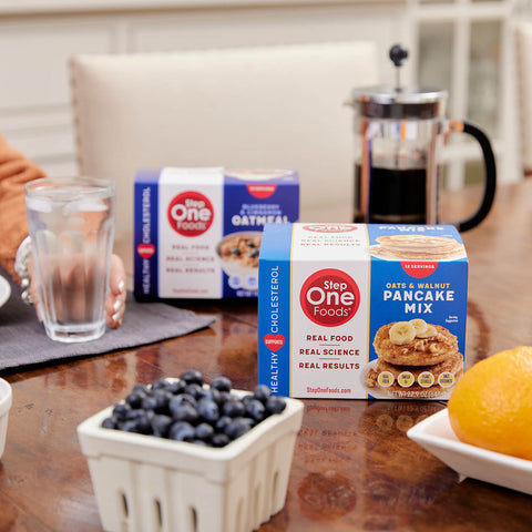 A box of Oats and Walnut pancake mix, and Blueberry Oatmeal on a table top with french press, blueberries, grapefruit, and a glass of ice water
