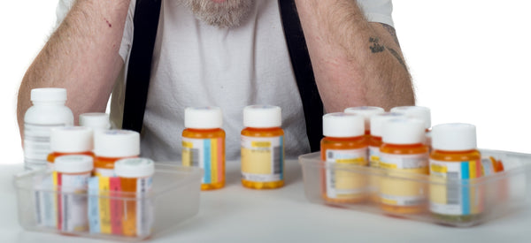 A man looking down at a handful of pills and prescription bottles