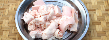 Raw chunks of beef fat in a stainless steel bowl, placed on a woven bamboo surface, prepared for rendering into beef tallow.