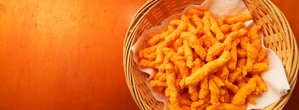 Cheetos in a wicker basket on a white napkin on a wooden table