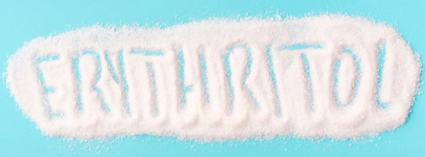 A spoonful of white erythritol sweetener beside processed diet foods