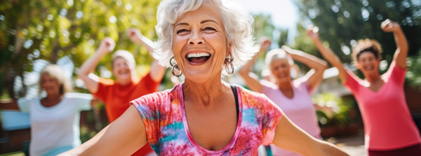 Smiling older woman in a colorful shirt exercising outdoors with a group of women.