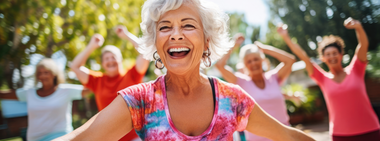 Smiling older woman in a colorful shirt exercising outdoors with a group of women.