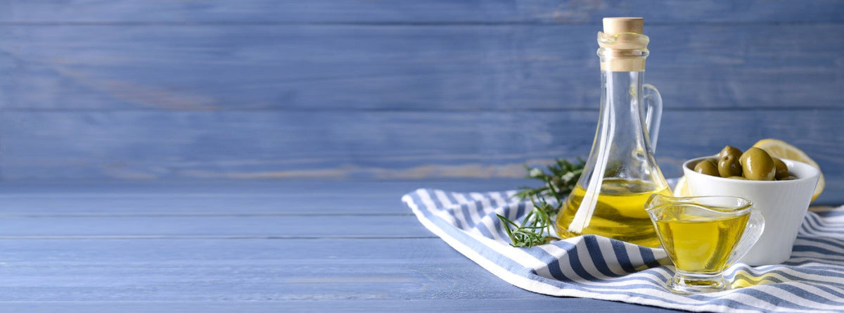 A glass cruet of olive oil beside fresh olives on a wooden table