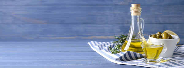 A glass cruet of olive oil beside fresh olives on a wooden table